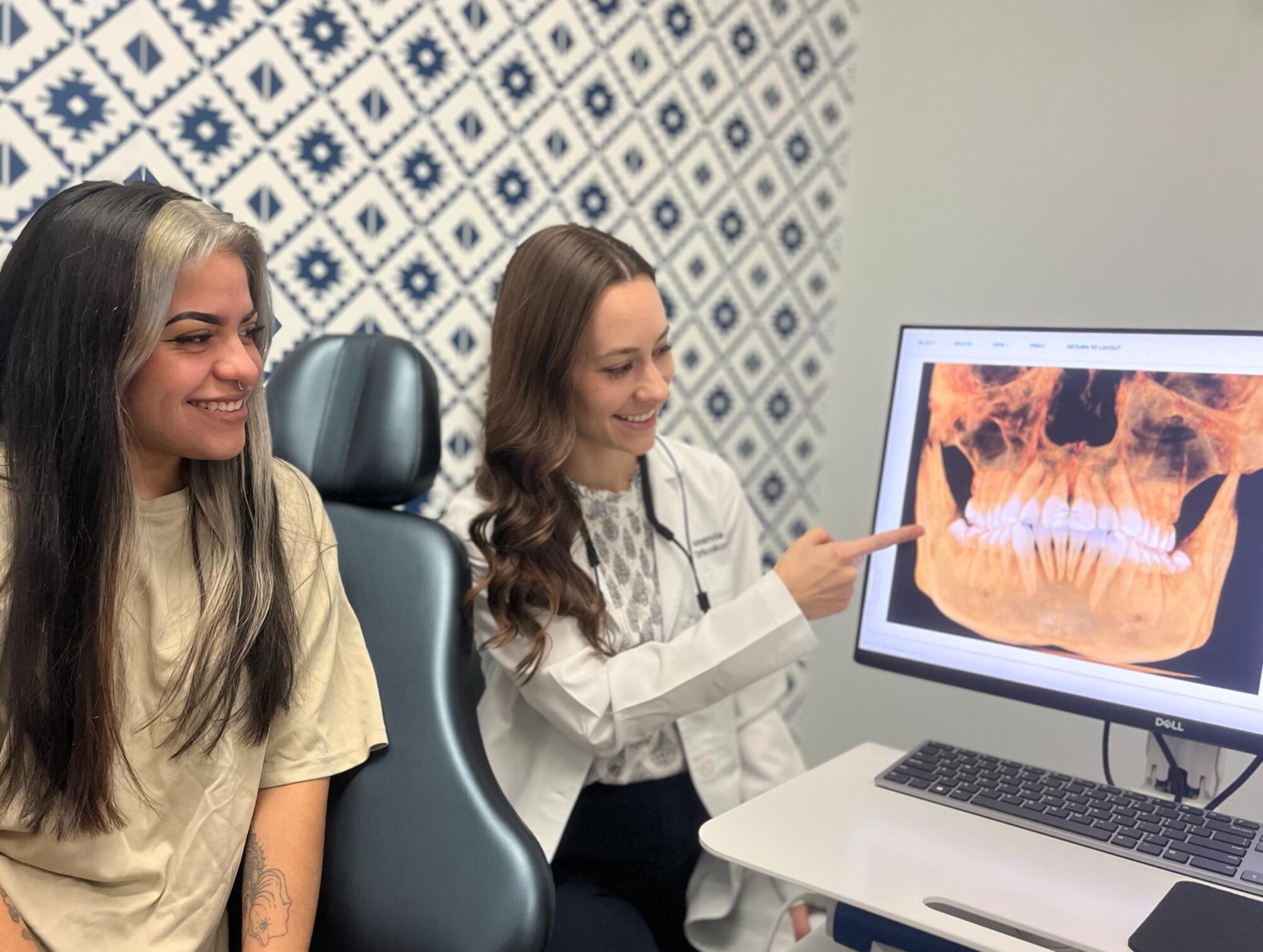 Patient and orthodontist discussing treatment options, viewing dental x-ray on monitor, in modern orthodontic office setting.