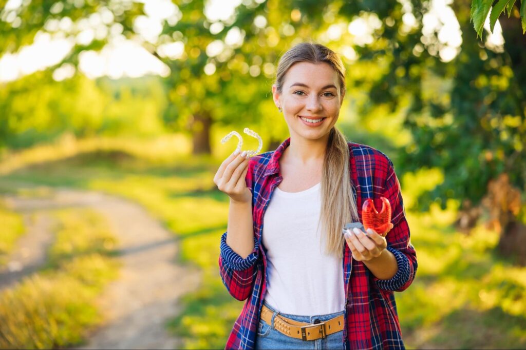 Young woman outdoors holding clear aligners and a model of teeth, representing orthodontic options for adults in El Paso.